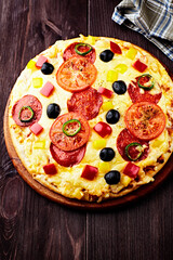 Pizza with salami, black olives, tomatoes and red, yellow and jalapeno pepper. Dark wooden background. Copy space.