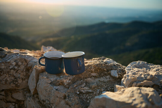 Two blue enamel coffee cups on rocky mountain top with scenic sunrise view