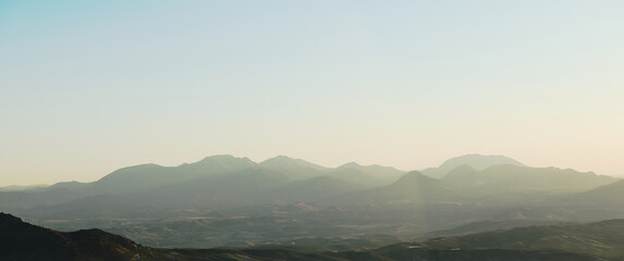 Panoramic view of serene mountain range at sunrise with mist and soft light