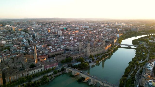 Panoramic aerial view of Zaragoza skyline. Orange sunset, sun in right corner of the camera. View of historic city center. River Ebro. Cathedral of Zaragoza in the middle. Drone forward descending.