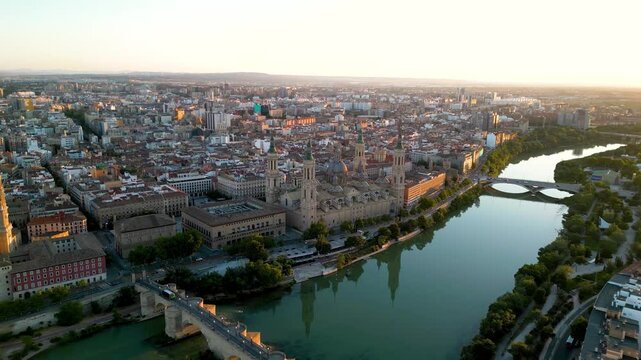 Panoramic aerial view of Zaragoza skyline. Orange sunset, sun in right corner of the camera. View of historic city center. River Ebro. Cathedral of Zaragoza. Forward.