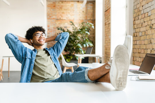 Cheerful mixed-race young man freelancer it marketing worker designer student manager intern relaxing listening music podcast e-book taking break at workplace in modern office loft cafe.