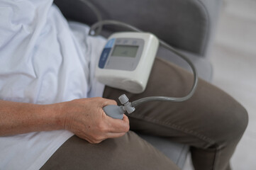 Mature Caucasian woman measuring blood pressure while sitting on sofa at home. 