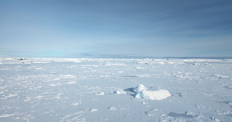 Frozen snow covered polar ocean surface under clear blue sky. White blanket desert land in Antarctica, winter landscape. Discover South Pole. Antarctic travel and exploration. Low angle drone flight