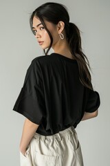 Fashion photo of an oversized black t shirt, worn in the style of an woman with dark hair and beige linen pants from the back view, white background, minimalistic style, focus on shirt, studio light,