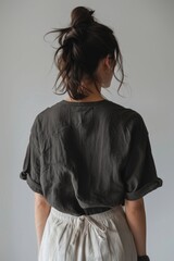 Fashion photo of an oversized black t shirt, worn in the style of an woman with dark hair and beige linen pants from the back view, white background, minimalistic style, focus on shirt, studio light,