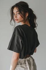 Fashion photo of an oversized black t shirt, worn in the style of an woman with dark hair and beige linen pants from the back view, white background, minimalistic style, focus on shirt, studio light,