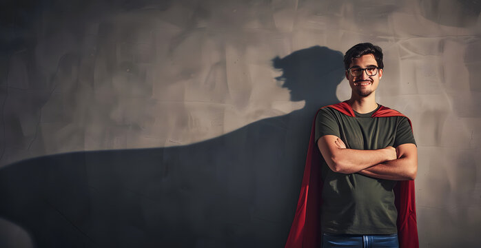 Confident young man keeps arms crossed smiling optimistic as casting a superhero with cape shadow on the wall. Motivated and ambitious guy tends to achieve success. Hero leadership and power concept