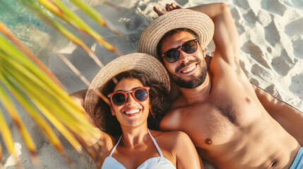 Happy couple sunbathing on a tropical beach under a palm tree