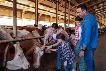 A happy family of farmers in a cowshed. A young married couple and their children take care of pets on the farm.