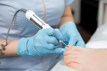 Podologist doing professional medical pedicure to young woman in the clinic.