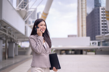 Attractive businesswoman talking on mobile phone walking in city street with skyscrapers cityscape background