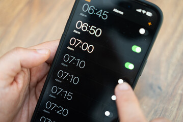 Person toggling alarms on a smartphone screen with a blurred wooden background. Efficient time management and daily scheduling concept. Perfect for technology and productivity themes 