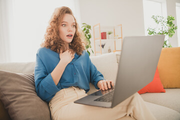 Photo of happy young girl sit sofa frightened reaction netbook blue shirt enjoy live new apartment room light house flat indoor