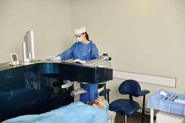 Doctor in scrubs performing surgery using a computer in a medical setting.