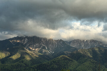 Tatra Mountains in Zakopane in spring, covered with cherished trees and remnants of snow from winter, big gray clouds enveloping the mountains