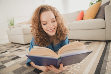 Full body photo of cheerful female lying floor read interesting book blue shirt enjoy weekend buy new apartment indoors inside house home © deagreez
