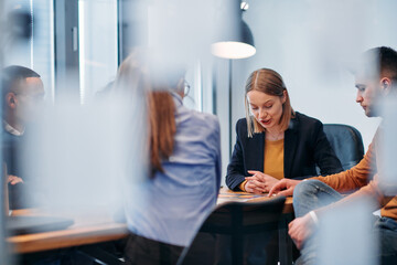 In a sleek glass office space, a team of business professionals engage in lively discussions and...