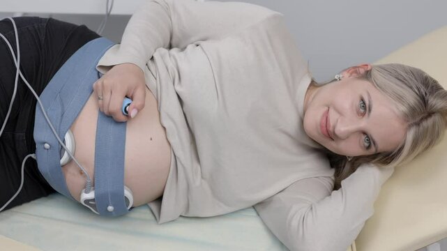 Woman pregnant checking fetal heart beat by fetal monitoring. Expectant mother with midwife adjusting sensors off cardiotocography