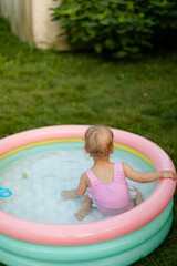 Baby in a pink swimsuit is swimming in inflatable pool in the backyard. No face. Back view. 