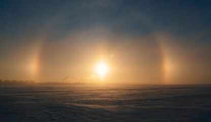 Halo effect around the sun during winter sunset over a vast snowy landscape