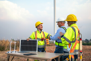 Engineer and manager in uniform shake hands and holding solar panels working teamwork in wind turbine farm, alternative renewable energy for clean power energy concept for the future.
