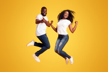 Jumping Black Millennial Couple In The Air, guy pointing at camera, yelllow background