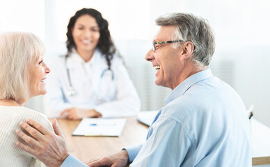 Obraz premium Good Diagnosis. Happy elderly couple looking at each other during consultation with female doctor at clinic, free space