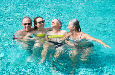 Group of four cheerful friends having fun in outdoor swimming pool under the sun. Vacation and relax concept