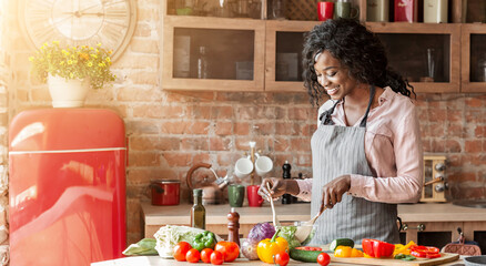 I care about my family. Attractive black woman cooking healthy veggies salad at kitchen, copy space