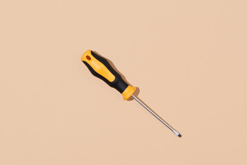 Screwdriver flat tip with yellow and black handle on beige background. Labor Day concept