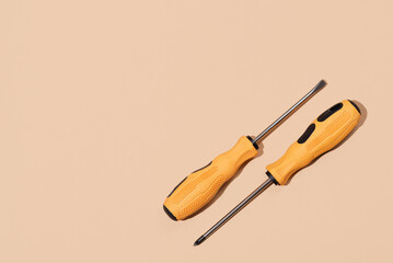 Two screwdrivers with yellow and black handle on beige background. Labor Day concept