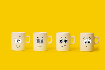 Tazas blancas con caras de cómicas sobre un fondo amarillo. Vista de frente y de cerca. Copy space