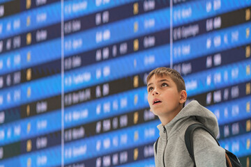 Young traveler with a backpack against the information board of departures and arrivals at the airport