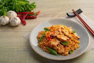 Spicy stir fried instant noodle with sliced pork meat and thai basil leaves in white plate
