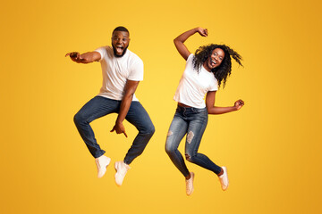 Super Excited Black Couple Leaping On Yellow Studio Background, having fun together