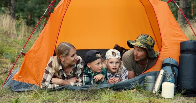 family with kids laying and talking in tent at forest campsite. nature adventure