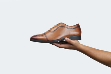tan leather oxford brogue shoes hold in hand isolated on white background