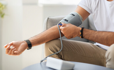 Closeup of unrecognizable male patient using modern tonometer at home, panorama with copy space. Cropped of middle-eastern man measuring his blood pressure, making self checkup