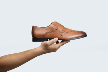 tan leather oxford brogue shoes hold in hand isolated on white background