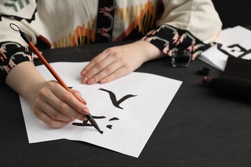 Calligraphy. Woman with brush writing words River and Entrance in Chinese on paper at black wooden...