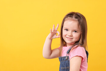 Portrait of cute little girl showing OK gesture on orange background, space for text