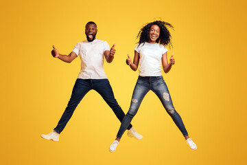 Happy Black Man And Woman Are Jumping In The Air And Showing Thumbs Up, yellow background