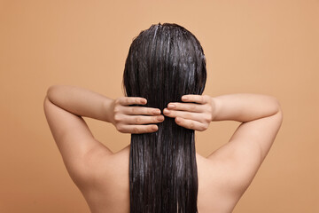 Woman applying hair mask on beige background, back view
