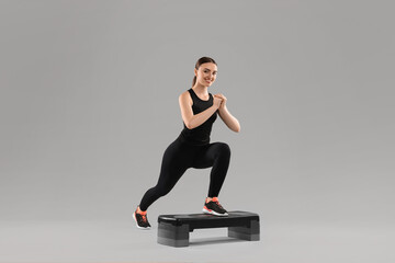 Young woman doing aerobic exercise with step platform on light background