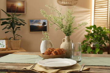 Clean tableware, flowers and fresh pastries on table in stylish dining room