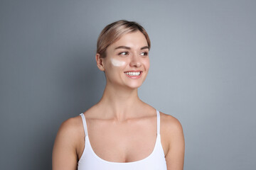 Fototapeta premium Beautiful woman with cream on her face against gray background