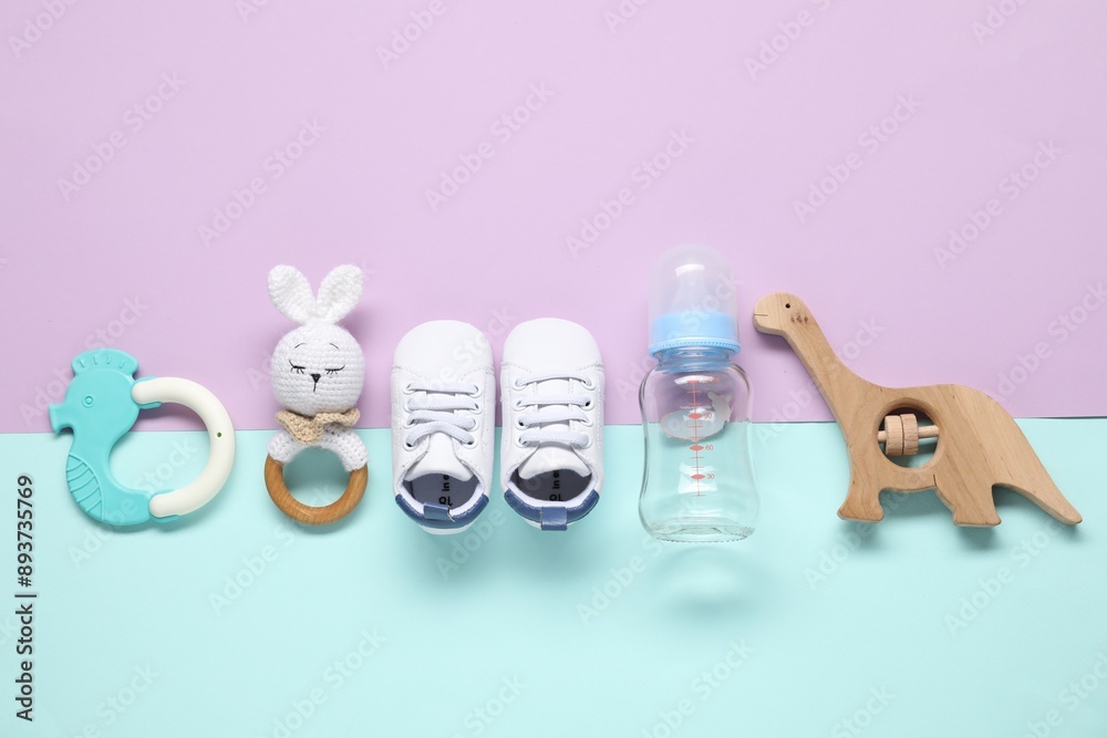 Wall mural Baby rattles, teether, bottle and booties on color background, flat lay