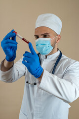 Male doctor wearing uniform mask and gloves look at blood in test tube isolated