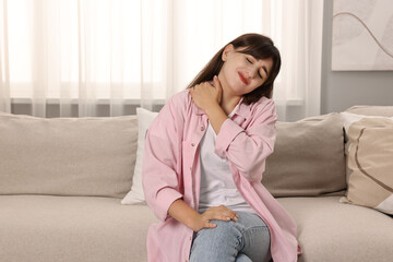 Upset woman suffering from neck pain on sofa at home